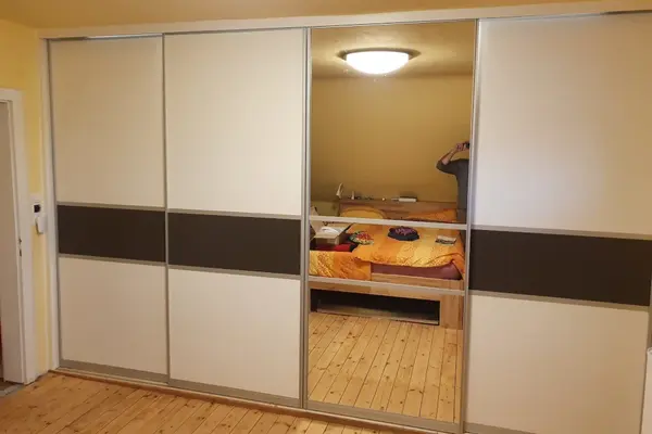 Großer Kleiderschrank mit Schiebetüren und Spiegel im Schlafzimmer auf Holzboden.